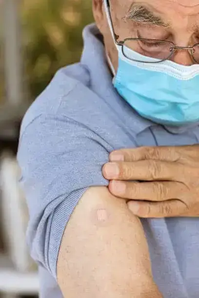 Senior man wearing a protective face mask is looking at his arm after vaccination.
