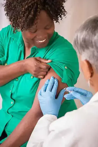 Senior adult doctor or nurse gives flu vaccine to African descent, mid-adult patient at a local medical clinic, hospital, or doctor's office.  NOTE:  This is a studio shot and not an actual medical clinic.